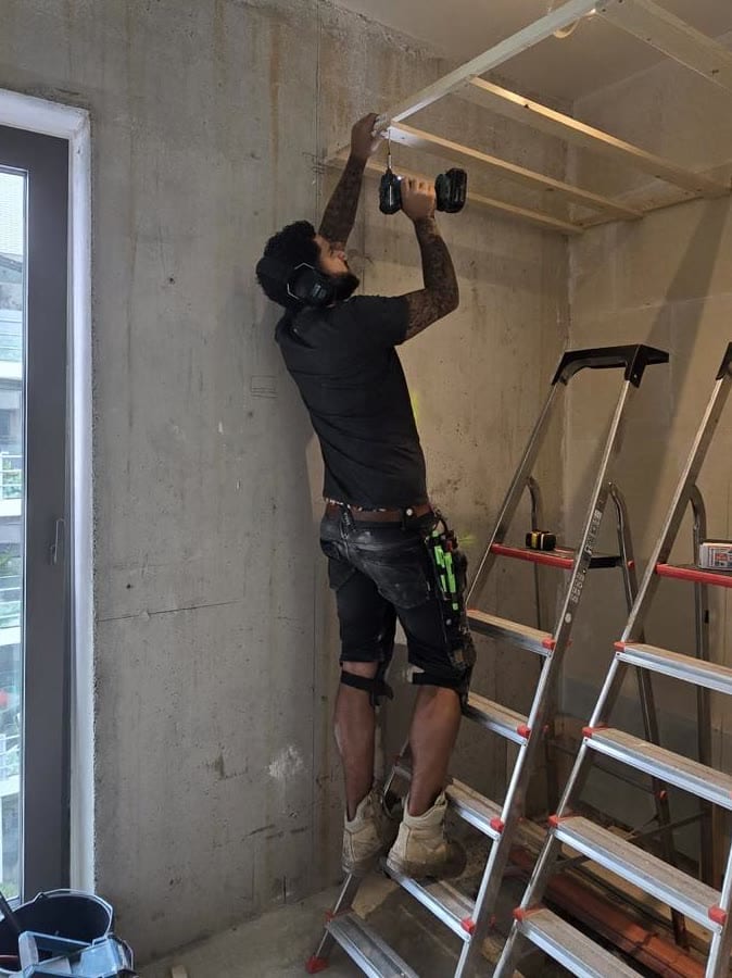 Sicil aan het werk op een trap bij het schroeven van regelwerk voor een plafond